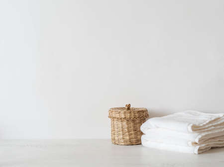 Wicker straw box and white towels on white background. Front view. Minimal bath background. Copy spaceの写真素材