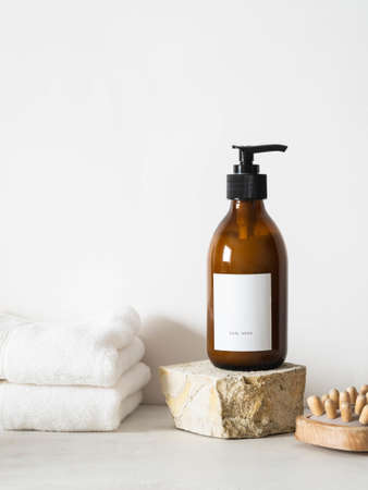 Cosmetic amber glass bottle with white lable on grange natural stone, wooden massager and white towels on white background. Front viewの写真素材