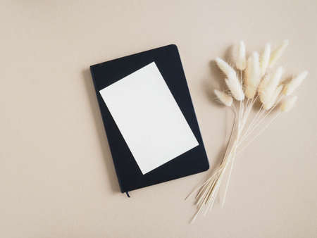 White blank card for text on black nptepad next to bouquet of dry Lagurus on beige background. Minimal concept for message, message or invitation in pastel colors. Top view. Copy space.の写真素材