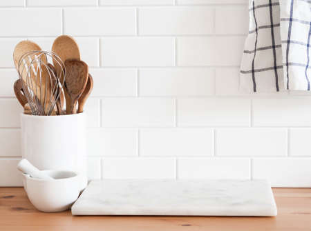 Stylish white kitchen background with kitchen utensils standing on wood countertop near white wall tiles, copy space for text, front viewの写真素材