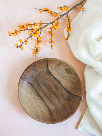 Round wooden craft plate mockup for eco, food or beauty product and branch with orange berries on pink background. Top view. Copy spaceの写真素材