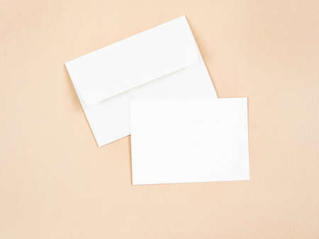 Empty white postcard and envelope on beige background. Holiday and invitation mockup. Copy space. Top viewの写真素材