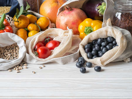 Fresh vegetables and fruits in eco cotton bags on table in the kitchen. Zero waste shopping concept. Front view. Copy space.の写真素材