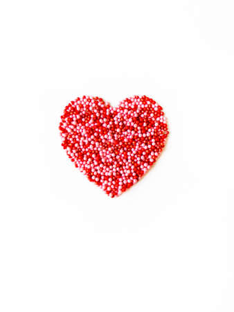 Valentine's card. Love heart made of red and pink pastry sprinkles on white background. Top view....