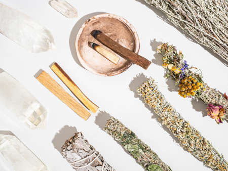 Items for spiritual cleansing - sage and aromatic herbs bundles, palo santo incense sticks and quartz crystals on white background. Top view. Flat layの写真素材