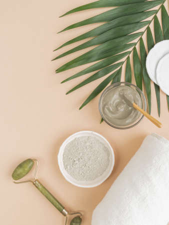 Homemade skincare concept. Organic blue clay for beauty facial mask, crystal massager, candle, cotton towel and palm leaf on beige background. top view. copy spaceの写真素材