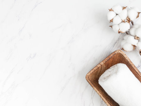 Minimal spa background or decor composition for advertising, cover. Cotton towels on wood tray and cotton branch on white marble background. flat lay. top view. copy spaceの写真素材