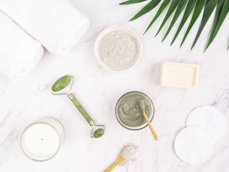 Homemade skincare concept. Organic blue clay for beauty facial mask, crystal massager, cotton pad, soap, candle, cotton towel and palm leaf on marble background. top view. copy spaceの写真素材