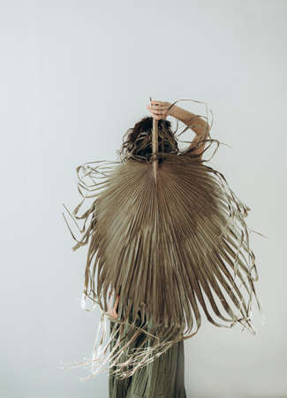 Unknown young woman holding dry palm leaf against white wall. Minimal beauty, fashion concept.の写真素材