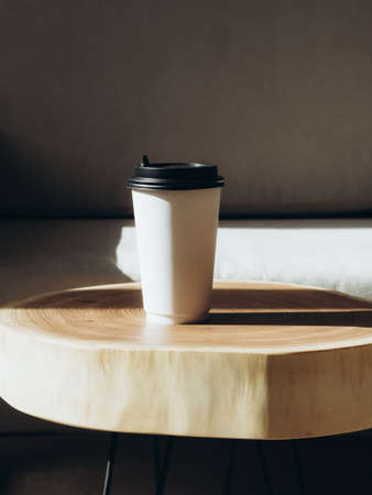Cup of coffee to go in white paper cup in sunlight on wood table. Morning coffee in cafe Place for text.の写真素材