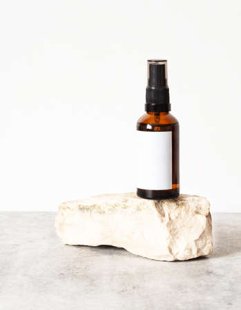 Mock-up of amber-colored glass bottle to natural stone. Facial serum, essential for care of women's skin on white background. front viewの写真素材