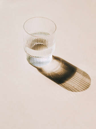 Glass of water and long shadow from sunlight on beige background. Minimal luxury modern concept. copy spaceの写真素材