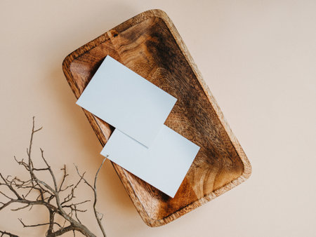 Two blank white cards on wooden tray and brunch of tree on beige background top view. Forms for business, advertising. Empty space for text. Minimal modern styleの写真素材
