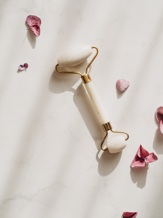 White Jade face roller for beauty facial massage therapy and pink Hydrangea flowers on white background with shadows. top view. copyspace.の写真素材