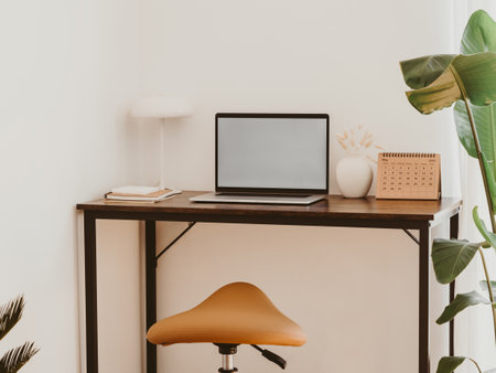 Stylish home office interior with laptop screen mockup, wooden table, plant, notes, saddle stool and elegant office accessories in designer apartment.の写真素材