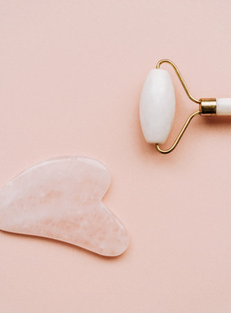 White roller and gua sha stone for facial massage on pink background. Home beauty and selfcare accessories. Face roller for anti age wrinkle treatment. Top view, flat lay.の写真素材