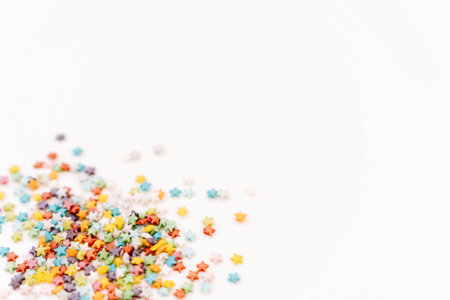 Colorful sugar confectionery stars scattered on a white background in food composition. Colored sugar sprinkles background, Sugar sprinkle dots, decoration for cake and bakery, a lot of sprinkles as a background. Top view