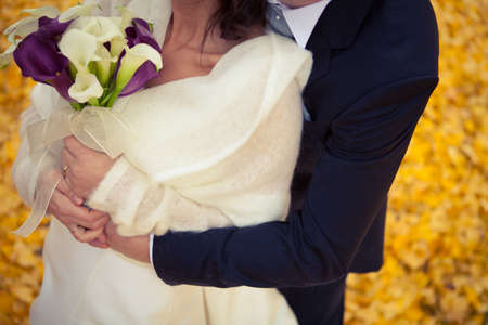Man in suit hug female in cream sweater holding lily flower bouquet outdoors in autumn backgroundの写真素材