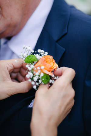 Close up female hand attach orange rose boutonniere. Mens wedding accessoriesの写真素材