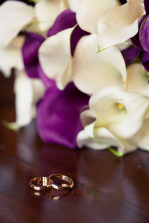 Two wedding rings with engraved wedding couple names lay on wooden surface with lily flower bouquet backgroundの写真素材