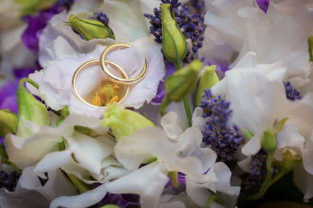 Close up female and male golden wedding rings lie on white flower petals on bouquet isolated floral backgroundの写真素材