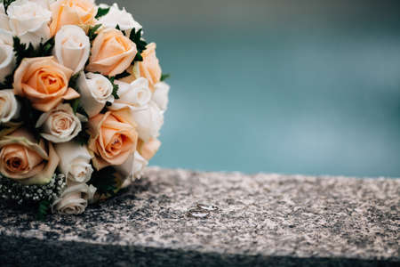 Close up golden wedding rings lay on hazelnut by bridal bouquet on gray ground surface. Flat-lay wedding photographyの写真素材