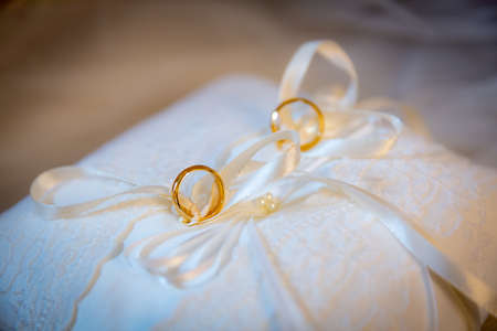 Two tiny golden wedding rings on white cushion on display for wedding ceremonyの写真素材