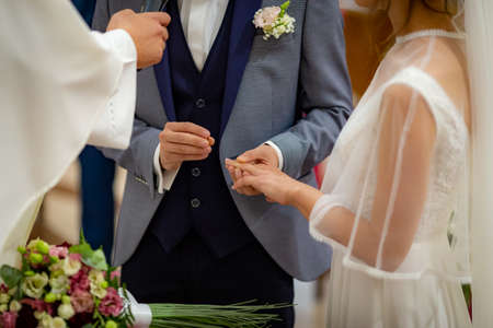Groom put wedding ring on brides finger in front of priest on wedding ceremonyの写真素材