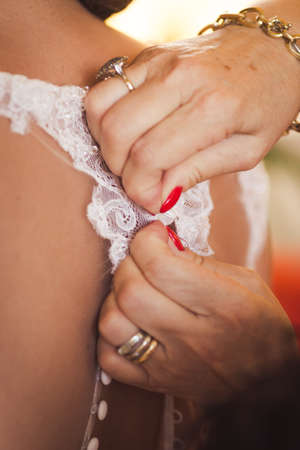 Bridesmaid helping bride in white dress to prepare her dress side view. Morning bridal preparation details newlyweds. Wedding day moments, wear white dress.の写真素材