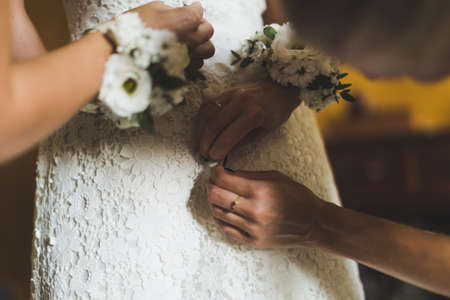 Two bridesmaids helping bride in white dress to prepare her dress back view. Morning bridal preparation details newlyweds. Wedding day moments, wear white dress.の写真素材