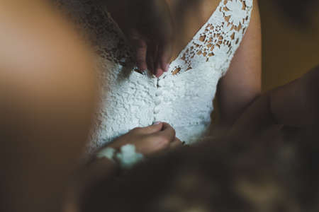 Two bridesmaids helping bride in white dress to prepare her dress back view. Morning bridal preparation details newlyweds. Wedding day moments, wear white dress.の写真素材
