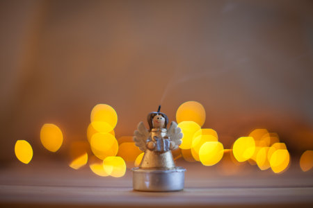 Burning candle in the shape of a Christmas angel and blurred Christmas lights as a background.の写真素材