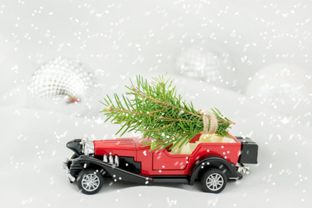 A red toy car carries spruce branches on a white blurry background. christmas card backgroundの写真素材