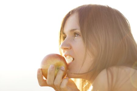 Beautiful young woman eating a red apple in bight sunの写真素材