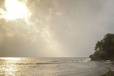 Golden sunlight sparkles on the surface of the sea next to natural coastline