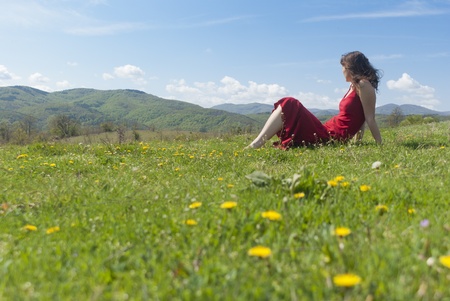 Beautiful young woman with red dress relaxing on a green meadow in springtimeの写真素材