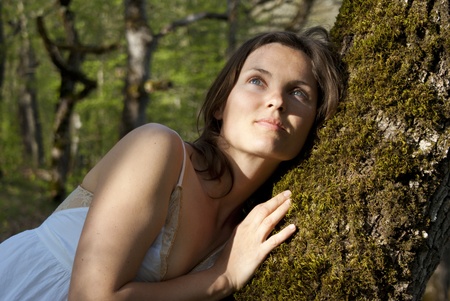 Beautiful young woman rests against a soft tree deep in the forestの写真素材