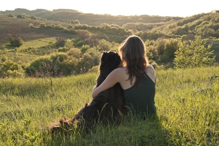 A beautiful young woman hugs her dog as they sit in a field の写真素材