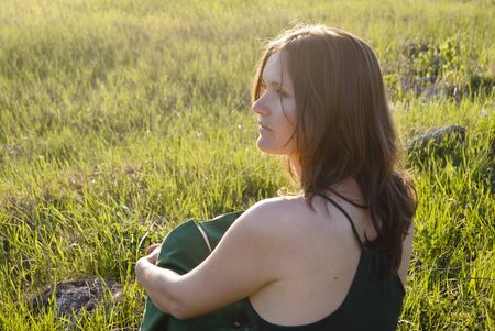 Young woman wearing green sits on the grass in the countrysideの写真素材