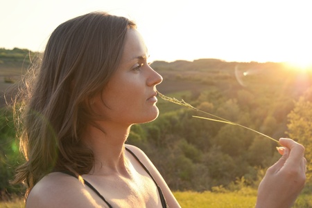 Beautiful young woman gently touches her lip with a long piece of grassの写真素材
