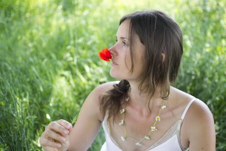 A beautiful young woman holds a poppy to her nose, sitting in a meadowの写真素材