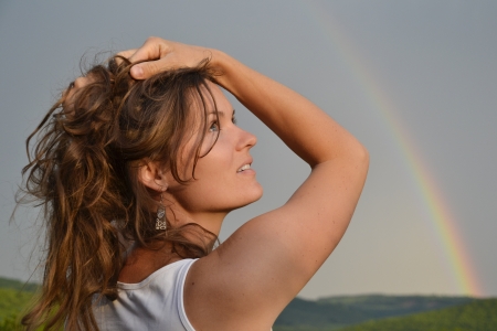 Beautiful young woman looking at the rainbow on the sky after the rain has passed and the sun has returnedの写真素材