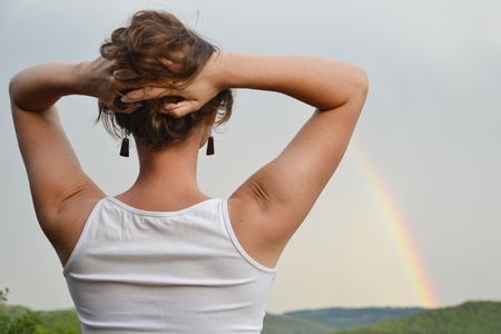Beautiful young woman looking at the rainbow on the sky after the rain has passed and the sun has returnedの写真素材