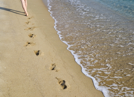 Female legs walking on the sandy beach washed by the surfの写真素材