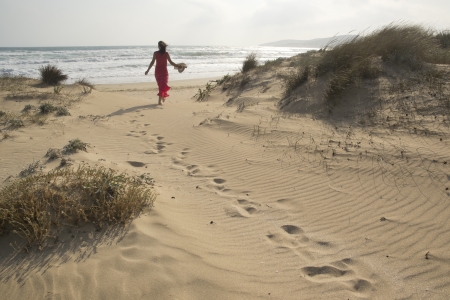 Beautiful young woman walking through the sand dunes towards  beachの写真素材