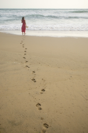 Beautiful young woman walking on the beach towards the sea leaving footprintsの写真素材