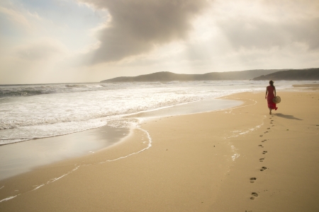 Young woman walk on an empty wild beach towards celestial beams of light falling from the skyの写真素材