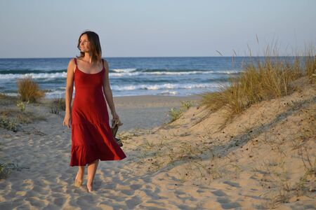 Beautiful young woman in a red dress walking back from the beachの写真素材