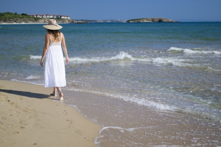 A beautiful young woman takes a relaxing walk along a sandy beachの写真素材