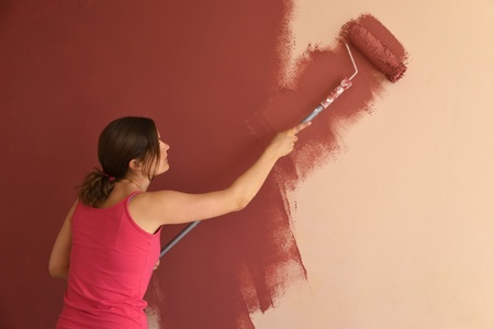 Beautiful young woman in causal clothes painting a wall with red paint and a rollerの写真素材